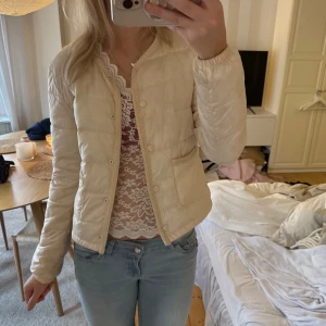 Beige quiltad pufferjacka - Säljer en beige pufferjacka med quiltad design och rund hals. Jackan har tryckknappar framtill och två fickor med snygga kantdetaljer. Lätt vadderad och perfekt för dig som gillar en clean och chill look. Passar till jeans och layering. Jag är en s men passar säker xs också 