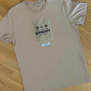 Beige Burberry t-shirt med patch - Storlek XXL men passar storlek M. Skriv om bild på hur den sitter. 
