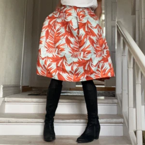 Vacker mönstrad kjol från H&M - Midilång kjol från H&M med ett tropiskt orange mönster på ljusblå bas. Kjolen har en A-linjeformad siluett, markerad midja och guldfärgad dragkedja bak. Materialet har en lyxig lite styv struktur som håller formen,  och modellen med fickor ger en cool känsla. Färgkombinationen är perfekt och passar super till vitt eller svart. Funkar året om beroende på hur den stylas. Modellen på bilden är strl 36/S och kjolen passar bra både till S/M. 