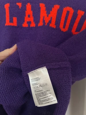 Lila stickad tröja L'AMOUR från Divided - Cool lila stickad tröja från Divided/HM med röd text 'L'AMOUR' = kärleken. Materialet är tunt stickad akryl. Hylla kärleken med detta statement plagg!