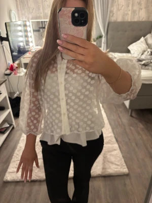 Vit prickig blus från Zara - Säljer en vit blus från Zara med stora prickar i transparent tyg. Blusen har voluminösa långärmar med resår vid ärmslut och knappar framtill. Den har en luftig och loose passform med ett extra lager tyg nedtill som ger en snygg volang-effekt.