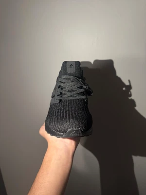 Svarta Adidas Ultraboost sneakers - Säljer ett par svarta Adidas Ultraboost sneakers i storlek 43 1/3. Skorna har stickad ovandel, platt sula och klassisk snörning. Boost-dämpning för extra komfort och en stilren, helsvart look med diskret Adidas-logga på plösen.
