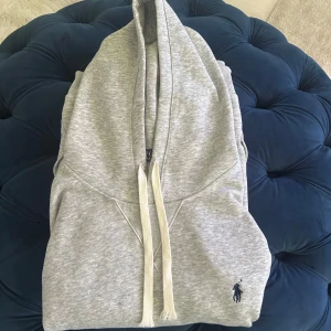 Grå hoodie från Polo Ralph Lauren - Snygg ljusgrå hoodie från Polo Ralph Lauren med klassisk broderad logga i mörkblått på bröstet. Väldigt bra skick-:9/10| Storlek -: M |. Riktigt stilig hoodie som passar till det mesta. Dma🤙 