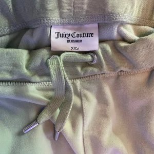 Juicy Couture ljusgröna mjukisbyxor XXS - Snygga ljusgröna mjukisbyxor från Juicy Couture i storlek XXS. Byxorna har snörning i midjan och är dekorerade med glittrande stenar som bildar texten 'Juicy' på baksidan. Perfekta för en chill och trendig look.