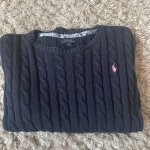 Mörkblå stickad tröja från Ralph Lauren - Säljer en snygg mörkblå stickad tröja från Ralph Lauren. Den har ett klassiskt flätmönster och en rosa logga på bröstet. Tröjan är långärmad och perfekt för kyligare dagar. Superbra skick och passar mig som har storlek XS/S annars. ( XL i barn storlek) 