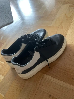 Alexander McQueen svarta och vita sneakers - Säljer ett par chunky Alexander McQueen sneakers i svart och vitt skinn med vit plattformssula. Skorna har rund tå, snörning och guldtext på hälen. Riktigt snygga och ikoniska, passar perfekt till streetwear och ger en cool vibe till outfiten. Släppt lite på sömmar men helt klart många promenader kvar och behagligt skön sko. 