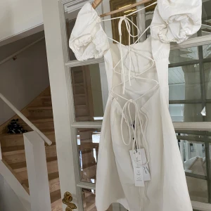 Vit kortklänning med snörning - Vit kort klänning som går att knyta i ryggen och justera så att den passar. Helt ny aldrig använd. Perfekt som studentklänning eller på sommaren annars