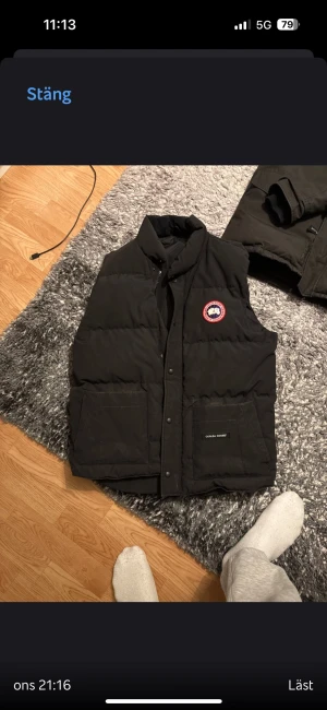 Svart dunväst från Canada Goose - Säljer en svart dunväst från Canada Goose med klassisk logga på bröstet. Västen har två stora fickor framtill, dragkedja och tryckknappar. Perfekt för lager-på-lager och riktigt skön när det är kyligt ute.