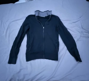 Mörkblå kofta från Pier One - Snygg mörkblå kofta från Pier One med hel dragkedja framtill och ribbad, grå krage. Tröjan har långärmad design och är tillverkad i mjukt bomullsmaterial. Perfekt för dig som gillar stilrena och bekväma plagg med enkel look.