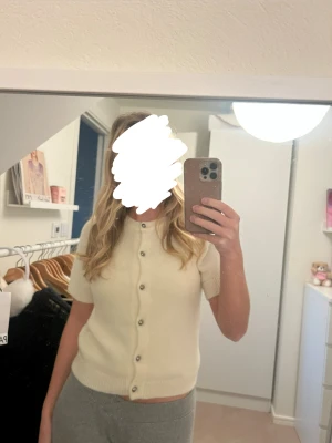 Kortärmad beige kofta med knappar - Säljer en söt och enkel beige kofta med korta ärmar och rund hals. Koftan har knappar hela vägen framtill och är stickad i mjukt material. 