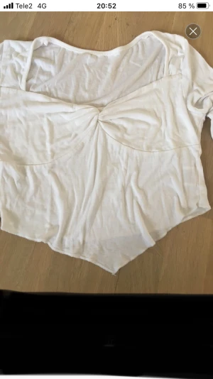 Vit croppad blus med trumpetärm - Säljer en vit blus med croppad passform och snygg twistad detalj framtill. Toppen har långa trumpetärmar och en v-ringad hals. Materialet är mjukt och lätt, perfekt för dig som gillar en chill och trendig stil.