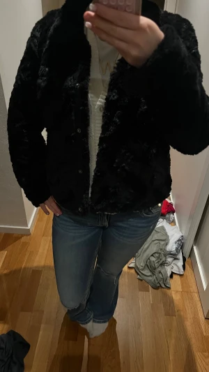 Svart pälsjacka med knappar - Säljer en svart pälsjacka med mjuk och fluffig känsla. Jackan har klassisk krage och stängs med knappar framtill. Passformen är normal och jackan är långärmad, perfekt för dig som gillar en stilren look med lite extra edge. Från veromoda!