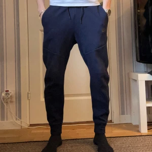 Mörkblå mjukisbyxor från Nike - Säljer ett par mörkblå Nike tech fleece byxor. Byxorna är i bra skick och är ritkigt snygga. Byxorna har även en ficka på sidan med zip. 