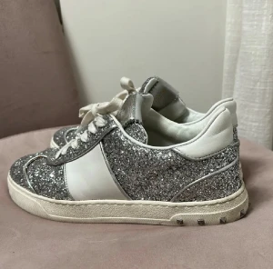 Valentino Garavani Flycrews  - Säljer ett par Valentino Garavani sneakers med silverglittrigt yttre, vita detaljer och snörning. Skorna har platt sula med nitar runt kanten, alla nitar är kvar. Inga defekter. 