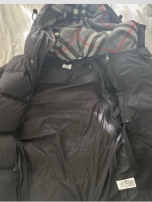 Svart dunväst/jacka från Burberry - Säljer en svart dunväst från Burberry med klassiskt rutigt foder i grått, rött och svart. Västen har dragkedja och knappar framtill, samt två sidofickor med dragkedja. Perfekt för lager-på-lager och har en schysst, puffig look. Pris ej hugget i sten! 