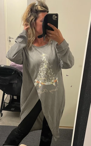 Grå långärmad jultunika med tryck - Säljer en grå långärmad låntröja/tunika  med ribbad struktur och ett glittrigt julgransmotiv framtill. Tunika har rund halsringning och omlott-detalj nedtill. Perfekt för dig som vill ha en mysig och snygg look till julen.Helt ny