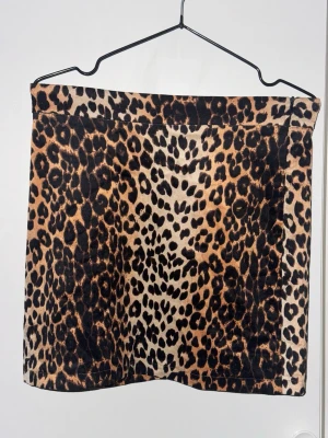 Leopardmönstrad kortkjol från NA-KD - Säljer en snygg kortkjol från NA-KD i storlek 36 med leopardmönster i bruna och svarta toner. Kjolen har en rak passform och är tillverkad i ett mjukt syntetmaterial som känns bekvämt mot huden. Perfekt för dig som vill sticka ut med en trendig look.