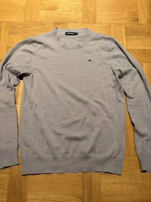 Grå stickad tröja från J.Lindeberg - Snygg grå stickad tröja från J.Lindeberg med rund hals och diskret logga broderad på bröstet. Tröjan har krympts i tvätten från M och sitter nu mera som S. Vid några frågor är det bara att höra av sig.
