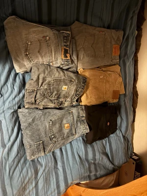 Mix av jeans till otroligt pris - Säljer ett gäng byxor: flera gråa och blåa Levi's jeans, två par Carhartt arbetsjeans i olika tvättar med klassiska fickor och logga, ett par beige Levi's jeans och ett par svarta Dickies arbetsbyxor. Perfekt för dig som gillar slitstarka och snygga byxor med cool vintagekänsla. Alla byxor kostar 1000+ nya. Du får alla för 800