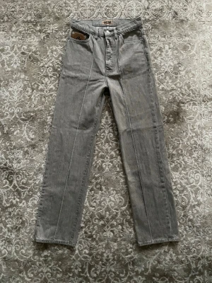 Grå jeans Corteiz - Säljer ett par grå jeans från Denim Gems med raka ben och snygga broderade detaljer på bakfickorna, bland annat en stjärna och ett C. Jeansen har normal passform, klassisk femficksdesign och är gjorda i bomull. Märkespatch i läder på fickan och midjan.