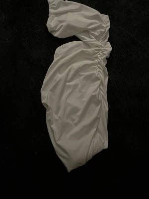 Vit omlottklänning med oneshoulder - Säljer en vit kortklänning med snygg omlott-design och oneshoulder. Klänningen har draperade detaljer längs sidan som ger en cool och modern look. Perfekt för dig som gillar stilrena och trendiga plagg. Materialet känns mjukt och har en lätt glans.