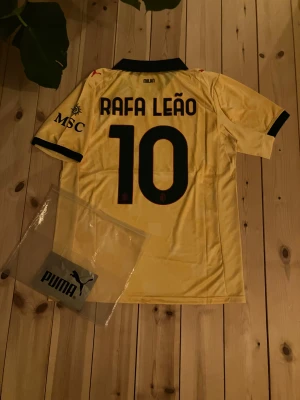 Leão ac Milan tröja - Bilderna visar en gul AC Milan fotbollströja med Rafa Leão och nummer 10 på ryggen, tillverkad av Puma. Ingen sko finns med på bilderna. TRYCK FELL