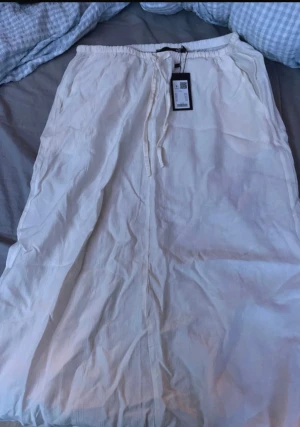 Vit långkjol med snörning - Säljer en fräsch vit långkjol med snörning i midjan, perfekt för varma dagar. Enkel design utan mönster.