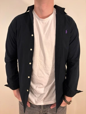 Svart Ralph Lauren skjorta - En stilren skjorta från Ralph Lauren. Second hand men i väldigt fint skick ✨ Tvättad och struken – redo att användas direkt.  Perfekt för vintern och nyår!🍾 Inga defekter och slim fit.  Storlek 👔: S Nypris 💰: ca 1 300 kr 