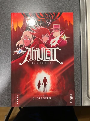 Amulett: Eldfågeln (Bok sju) - Följ med på ett episkt äventyr i den sjunde delen av Amulett-serien! Mystiska krafter, farliga hemligheter och spännande miljöer väntar när Emily och hennes vänner kämpar mot mörka hot. Perfekt för dig som gillar action, fantasy och snygga tecknade serier.