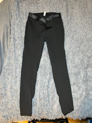 Svarta Ultimate Training V-Shape Tights från ICANIWILL - Säljer ett par svarta leggings från ICANIWILL med bred elastisk midja och logga. Materialet är stretchigt med 78% återvunnen polyester och 22% spandex, vilket gör dem riktigt sköna och följsamma. Perfekta för träning eller chill.  silikonremsor på insidan av midjan för extra grepp. Nypris 799kr