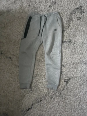 Grå mjukisbyxor från Nike och Nike kofta  - Säljer koftan och byxorna. Byxorna har små okej fläckar klor setter för 3000.Eftersom jag andvänt de Säljer för 550.
