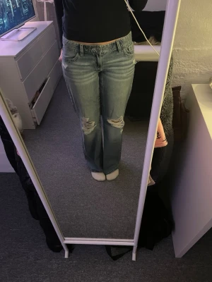 Blå lågmidjade baggy jeans från Gina Tricot - Ljusblå jeans från Gina Tricot med slitna knän och rosa detaljer på bakfickorna. Dom är baggy men sitter tajt vid midjan och är väldigt mjuka och sköna, använda en gång. Dom passar mig bra som är 172cm och går hela vägen ner.