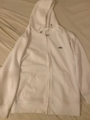 Vita mjukisbyxor från Lacoste - Säljer ett par vita mjukisbyxor från Lacoste med klassisk krokodillogga broderad på benet. Byxorna har snörning i midjan, muddar vid bensluten och är gjorda i mjukt bomullsmaterial. Regular fit som sitter skönt och avslappnat.