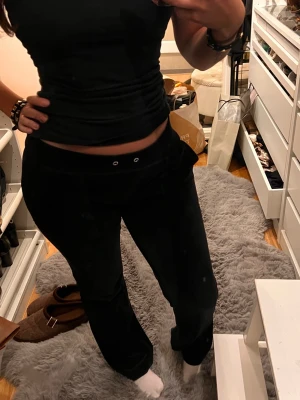 Svarta mjukisbyxor med fickor - Svarta mjukisbyxor med silverfärgade knappar på bakfickorna och detaljer vid midjan. Byxorna har en loose passform och är tillverkade i velour.