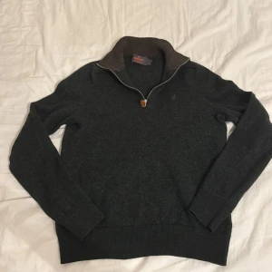 Mörkgrön merinoullströja från Morris - Snygg mörkgrå tröja från Morris i 100% merinoull med halv dragkedja och hög krage. Broderad logga på bröstet och ribbade muddar. Perfekt för lager-på-lager och chill höst- eller vinterstil