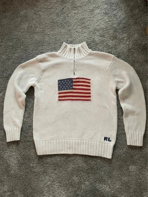 Vit stickad tröja med amerikansk flagga - Hej! Säljer en Ralph lauren quarter zip med cabelsticksd USA flagga. Har en pytte liten fläck längst ner syns knappast vid användning. skriv för mer bilder. Storlek XS