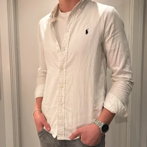 Vit skjorta från Ralph Lauren - Vit långärmad skjorta från Ralph Lauren med klassisk krage och knappar framtill. Skjortan har den broderade loggan på bröstet och är gjord i mjuk bomull. Passformen är normal. Använd fåtal gånger. Sitter som XS-S.