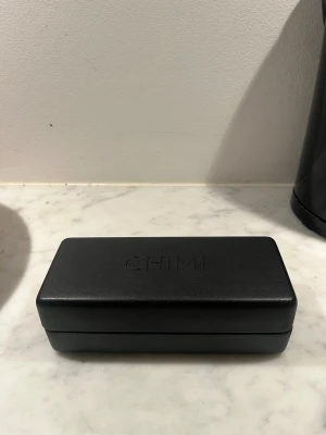 Svart CHIMI CORE 10 solglasögon - Säljer ett par svarta CHIMI CORE 10 solglasögon, Rektangulär form med breda bågar. Kommer med original  fodral och tygpåse. Perfekt accessoar för dig som gillar minimalistisk design. Aldrig använda då de inte passar på mig. 