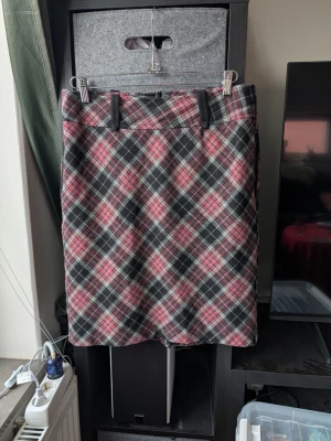 Rutig kjol från Great Rumors - Säljer en snygg rutig kjol från Great Rumors i storlek 38. Kjolen har svart, grå och röd färg med klassiskt rutmönster och bälteshällor upptill. Materialet känns som ullblandning och kjolen har dragkedja bak. Perfekt för dig som gillar preppy stil!