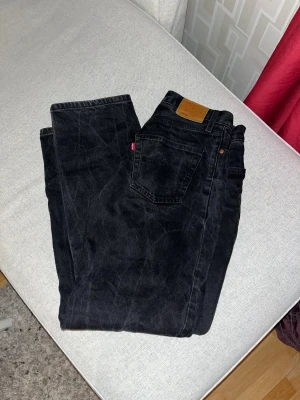 Levi's 505 svarta jeans - Svarta Levi's 505 jeans med klassisk femficksdesign och brunt läderpatch bak. Jeansen är raka i modellen och har en cool, mörk tvätt. Tillverkade i slitstark bomull och har Levi's Premium-märkning på insidan. 