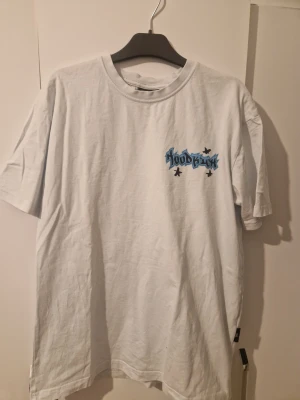Vit Hoodrich t-shirt med graffiti-tryck - Vit t-shirt från Hoodrich i storlek S med flera coola graffiti-inspirerade tryck i blått och svart både fram och bak.orginal färgen är vit MEN färgades av tiöl LJUS LJUD blå men syns inte .T-shirten har rund hals och korta ärmar, tillverkad i mjuk bomull. Perfekt för dig som gillar streetwear och vill sticka ut med en unik design.