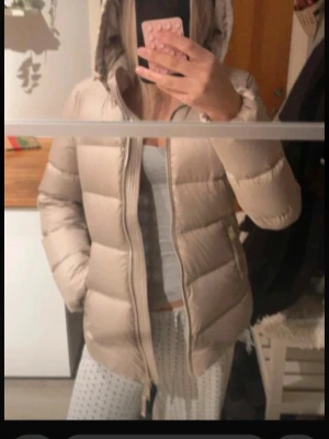 Beige pufferjacka från Massimo Dutti - Säljer en beige pufferjacka från Massimo Dutti med huva och dragkedja framtill. Jackan har en quiltad design och är tillverkad i polyester, perfekt för kyliga dagar. Snygg och enkel att matcha med olika outfits.