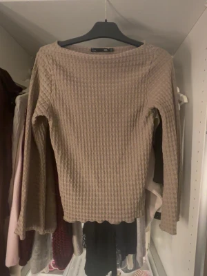 Beige långärmad topp från 157 - Säljer en beige långärmad topp från 157 i storlek XS. Toppen har ett våfflat, ribbat mönster och är tillverkad i ett mjukt syntetmaterial. Rund halsringning och vågig kant nedtill ger en chill och modern vibe.