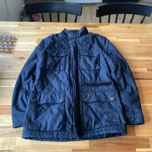 Mörkblå quiltad jacka - Säljer en mörkblå quiltad jacka med dragkedja och knappar. Jackan har flera fickor med knappdetaljer och en hög krage. Perfekt för kyligare dagar.S i storlek men passar även M! 9/10 skick knappast använd inga defekter alls!