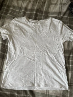 Vit t-shirt från 157 i bomull - En klassisk vit t-shirt från 157 i storlek S, tillverkad i 100% bomull. Modellen har rund hals och korta ärmar, perfekt för en enkel och clean look. Passar dig som gillar basic och stilrena plagg.