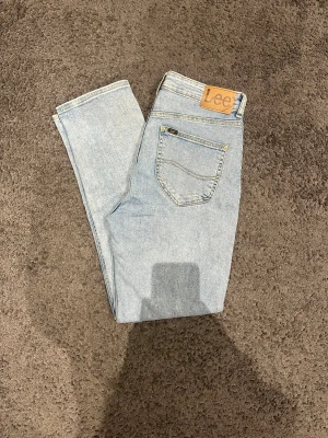 Ljusblå Lee jeans med rak passform - Säljer ett par ljusblå jeans från Lee med klassisk rak passform och fem fickor. Jeansen har hög midja och är tillverkade i slitstarkt bomullsmaterial. Snygga kontrastsömmar och Lee-lapp baktill ger en tidlös look. Perfekta för dig som gillar enkel och clean stil. Lappen har släpp lite men annars perfekta. Pris går att diskutera. 105 cm långa. 