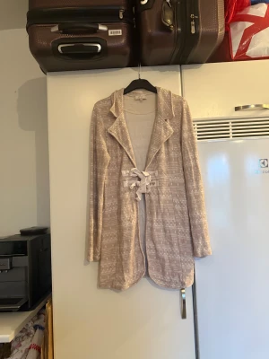 Beige kofta med knyt från Cream - Superfin beige kofta från Cream med snyggt mönster och knytband framtill. Långärmad och i mjukt material, perfekt för lager på lager. Koftan har en avslappnad passform och coola detaljer som ger en unik look. Storlek M. Mer använd men fint skick, kan finnas tecken på användning. 