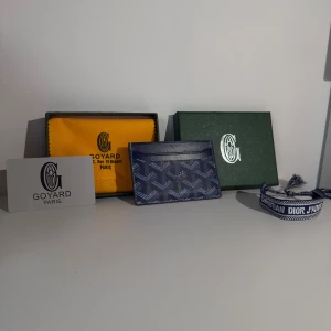 Blå  plånbok med mönster och ett blått armband - Supersnygg blå plånbok med ikoniskt grafiskt mönster i vitt och mörkblått. Slimmad design med flera fack för kort, perfekt att ha i fickan eller väskan. Gjord i exklusivt skinn och levereras med originalförpackning.