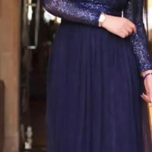 Marinblå långklänning med glitter - Snygg marinblå långklänning med glittrig överdel och långärmade ärmar. Kjolen är mjukt fallande och ger en elegant siluett. Perfekt för dig som vill sticka ut med lite extra glam på nästa bal eller fest.