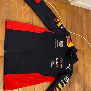 Puma Jacka redbull  - Snygg Red Bull Racing jacka från Puma i mörkblått och rött med loggor från Aston Martin, Honda och flera sponsorer.  Helt oanvänd, säljs inte längre. Går för runt 1000kr